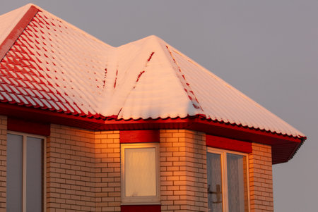 Roof of a house covered in snow at sunset.