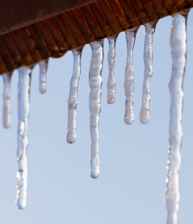 Icicles hang from the roof against the blue sky.