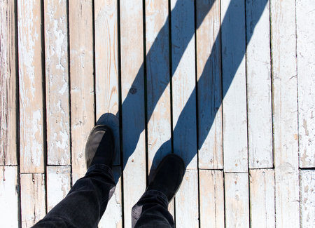 Shadow of a man's feet on a wooden floor.の写真素材
