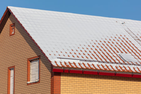 Roof of a house covered in snow against a blue sky.の写真素材