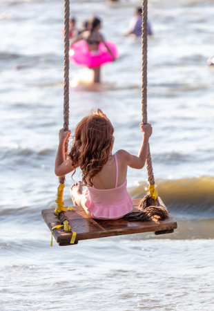 A girl rides on a swing on the seashore.の写真素材