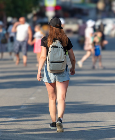 A girl in shorts with a backpack walks along the road.の写真素材