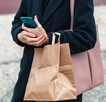 A woman with a paper bag and a phone in her hands.の写真素材