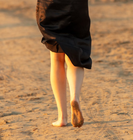 A girl in a black skirt with bare feet walks along the sand by the sea. Sunset.の写真素材