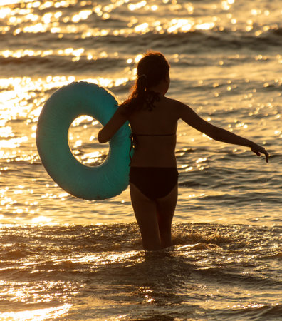 A girl with a circle swims in the sea at sunset.の写真素材