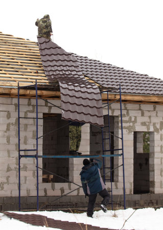 Workers install tiles on the roof of a house in winter.の写真素材