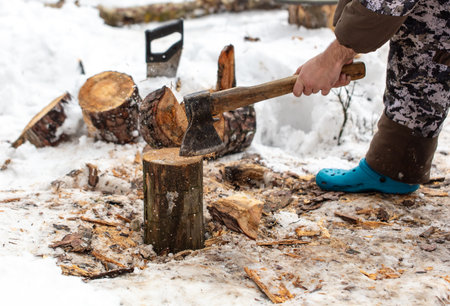 A man chops wood with an ax in the snow in winter.の写真素材