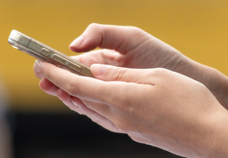 Phone in the hands of a woman on a yellow background.