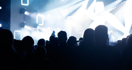 Silhouettes of spectators against a background of blue light at a concert.