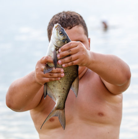 Bream fish in the hands of a boy on the shore of the lake.の写真素材