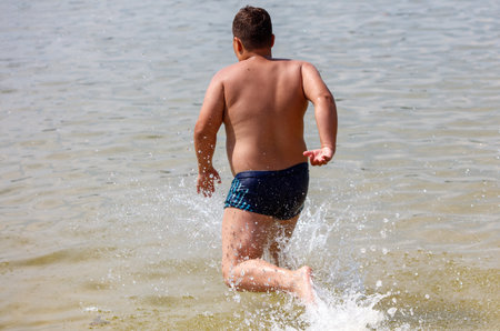 A boy runs through the water of the sea and jumps into the water.の写真素材