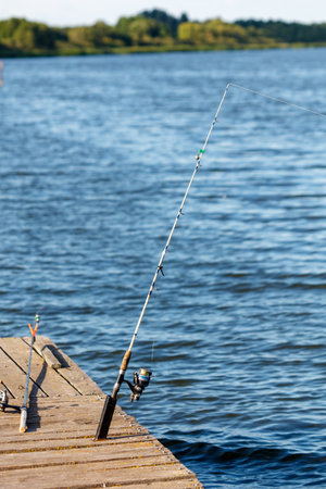 A fisherman's fishing rod on a wooden bridge on a lake.の写真素材