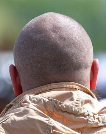 A man with a shaved head is wearing a tan jacket. The jacket is made of a light material and has a hood. The man's head is bald, and he has a beard. Scene is casual and relaxedの写真素材