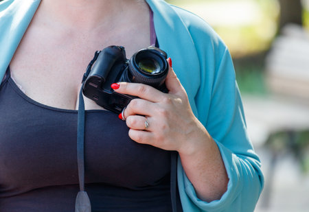 A woman is holding a camera in her chest. The camera is black and silver. The woman is wearing a...