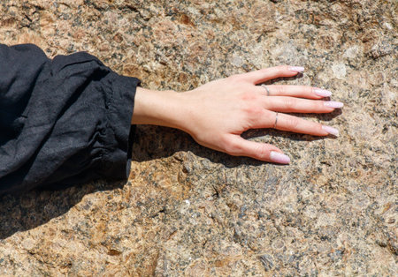 A woman's hand is resting on a rock, with her nails painted and a ring on her fingerの写真素材