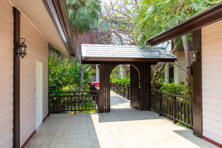 A walkway with a wooden archway leading to a building. The archway is decorated with plants and the walkway is paved with tilesの写真素材