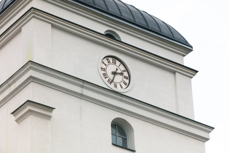 A clock tower with a white clock face and roman numeralsの写真素材