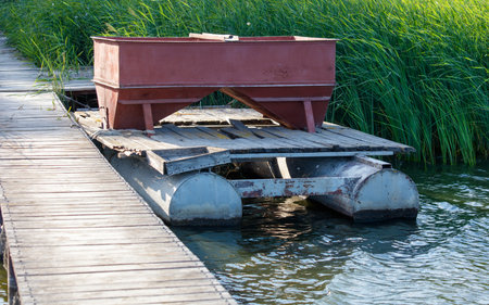 A boat is sitting on a dock with a red container on top of it. The container is open and the boat is partially submerged in water. The scene has a calm and peaceful mood, with the boatの写真素材