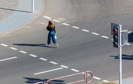 A woman is walking across a street at a crosswalk. The street is empty and the traffic light is red
