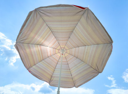 A large umbrella with a white and yellow striped canopy is open on a sunny day. The umbrella is...