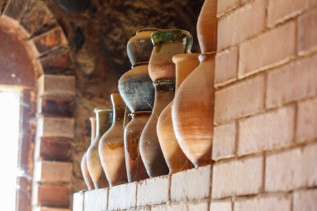 A row of old clay vases sit on a brick shelf. The vases are of various sizes and colors, and they appear to be quite old. The scene gives off a sense of nostalgia and historyの写真素材