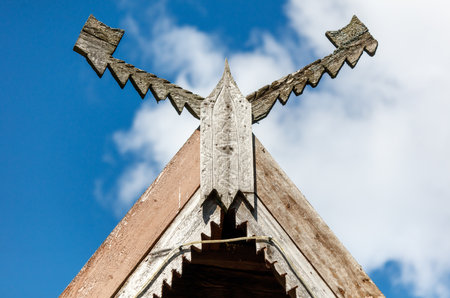 A wooden roof with a cross on top of it. The cross is pointing to the sky. The roof is old and has a weathered look. The sky is blue and clearの写真素材