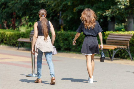 Two women walking down a sidewalk, one of them carrying a purse. Scene is casual and relaxed