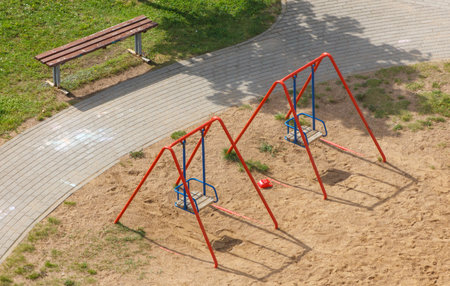 A park with a playground and a dirt area. The playground has a merry-go-round and a swing set