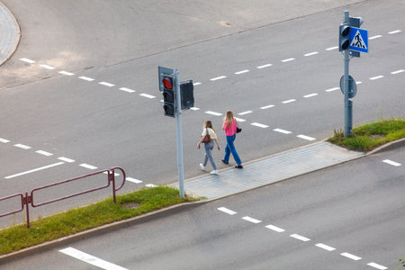 Two women cross a street at a crosswalk. The street is empty and the traffic lights are red