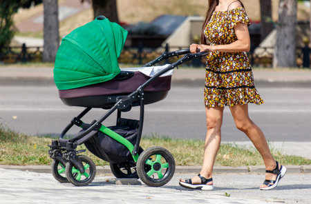 A woman is pushing a stroller with a green canopy. She is wearing a yellow and black dress
