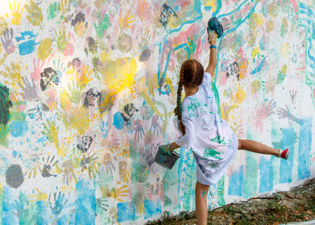 A girl is painting a wall with her hands and a brush. The wall is covered in handprints and the girl is adding her own. Scene is playful and creativeの写真素材