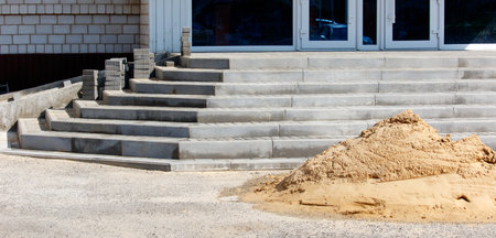 A pile of sand is next to a set of stairs. The stairs are made of concrete and are in the process of...