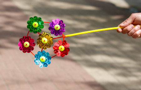 A hand holding a colorful flower toy. The toy is made of plastic and has a yellow stemの写真素材