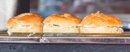 Three sandwiches are on a metal tray. The sandwiches are cut in half and are sitting on a counter