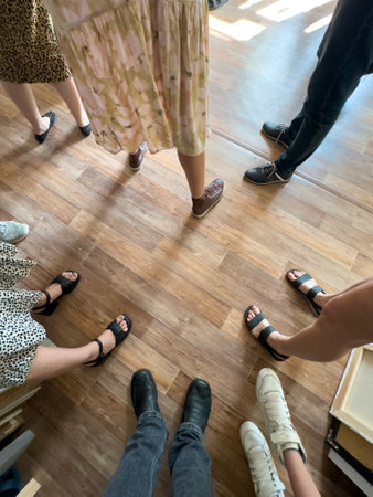 A group of people standing in a circle on a wooden floor. Scene is lighthearted and fun, as the...