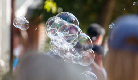 A group of people are standing in front of a house with a large bubble in the air. The bubble is surrounded by other bubbles, creating a colorful and playful atmosphereの写真素材