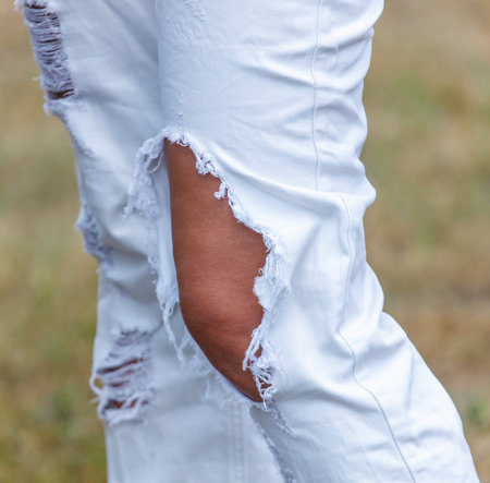 A person is wearing ripped white pants. The pants are torn in the knee areaの写真素材