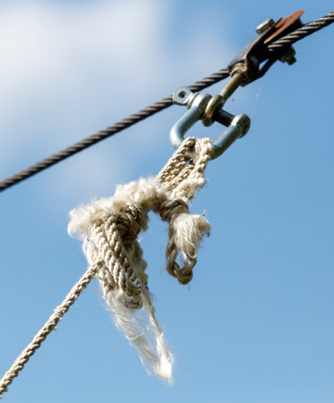 A rope is hanging from a wire and is frayed. The rope is white and has a few knots
