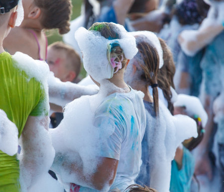 A group of people are playing in a pool of foam. A girl is in the middle of the group and has her head covered in foamの写真素材