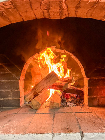 A fire is burning in a brick oven. The fire is orange and yellow, and the logs are stacked in a pile. The oven is open, and the fire is hotの写真素材
