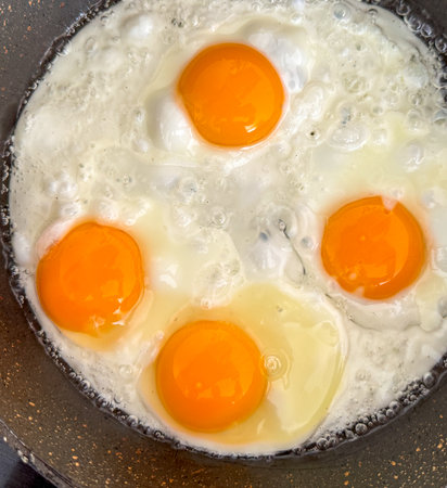 A pan of eggs is cooking on a stove. The eggs are in different stages of cooking, with some still runny and others already cooked. The pan is black and shinyの写真素材