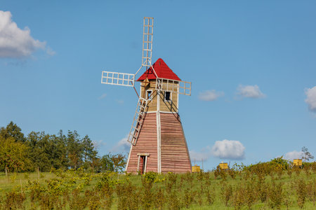 A windmill is standing in a field with a blue sky in the background. The windmill is old and has a...