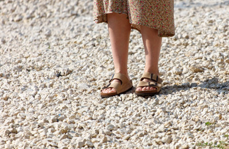 A woman is standing on a rocky surface wearing sandals. Concept of relaxation and leisure, as the woman is enjoying the outdoors. The rocky terrain adds a naturalの写真素材