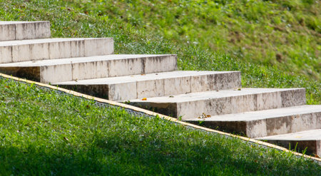 A set of concrete steps leading up to a grassy hill. The grass is green
