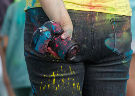 A woman is holding a camera with colorful paint on it. The camera is in her hand and the paint is all over her jeans. The scene seems to be a playful and creative momentの写真素材