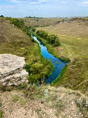 A river runs through a grassy valley with a rocky outcropping on the side. The water is clear and...