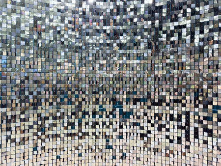 A wall of shiny silver tiles with a pattern of squares. The tiles are reflective and create a sense...