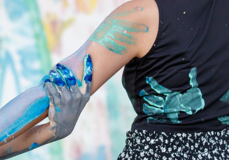 A woman with blue and gray paint on her arms and hands. The woman is wearing a black shirt and black pantsの写真素材