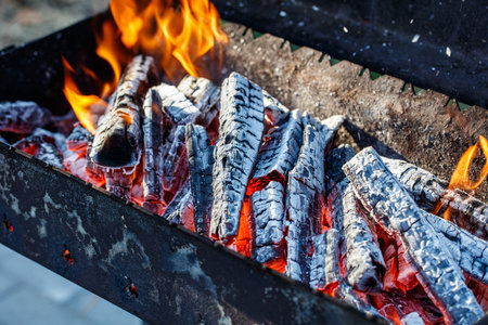 A grill with a pile of wood on it, and the wood is burning. The fire is hot and bright, and the wood is charred and black. Scene is intense and dramaticの写真素材