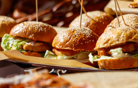 A tray of hamburgers with lettuce and sesame seeds. The hamburgers are on a paper plate and are sitting on a tableの写真素材